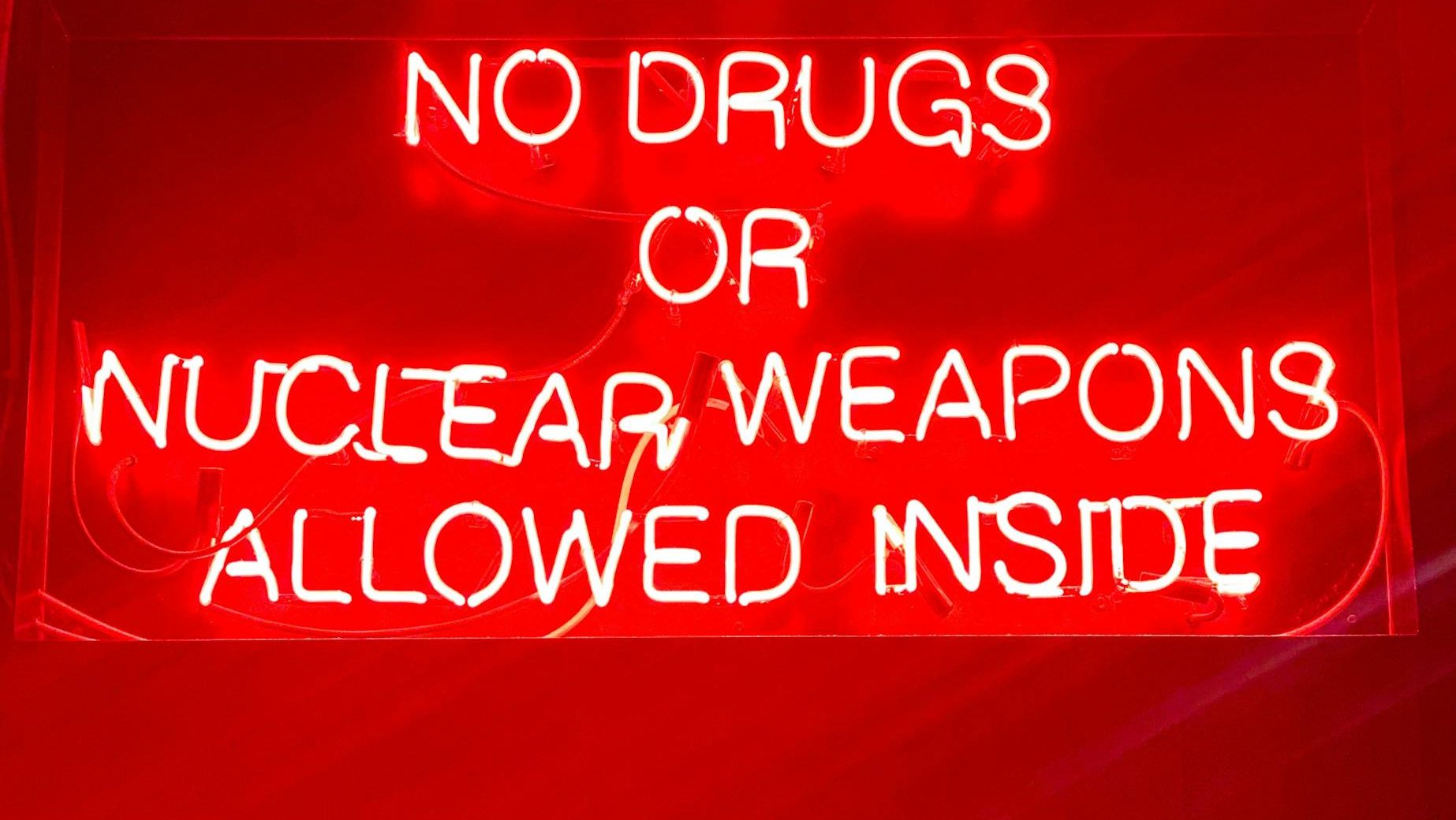 Bright neon sign reading 'No drugs or nuclear weapons allowed inside' in a bar setting.